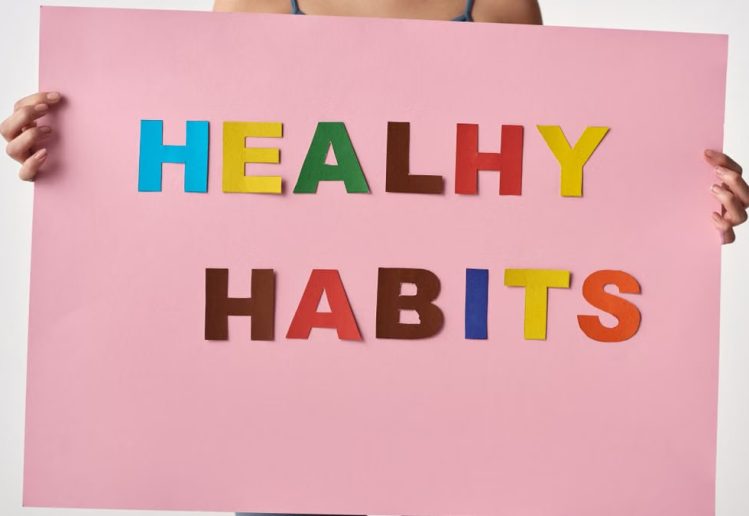 A woman holds a pink poster with colorful letters spelling 'HEALTHY HABITS'.