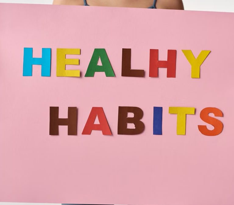 A woman holds a pink poster with colorful letters spelling 'HEALTHY HABITS'.